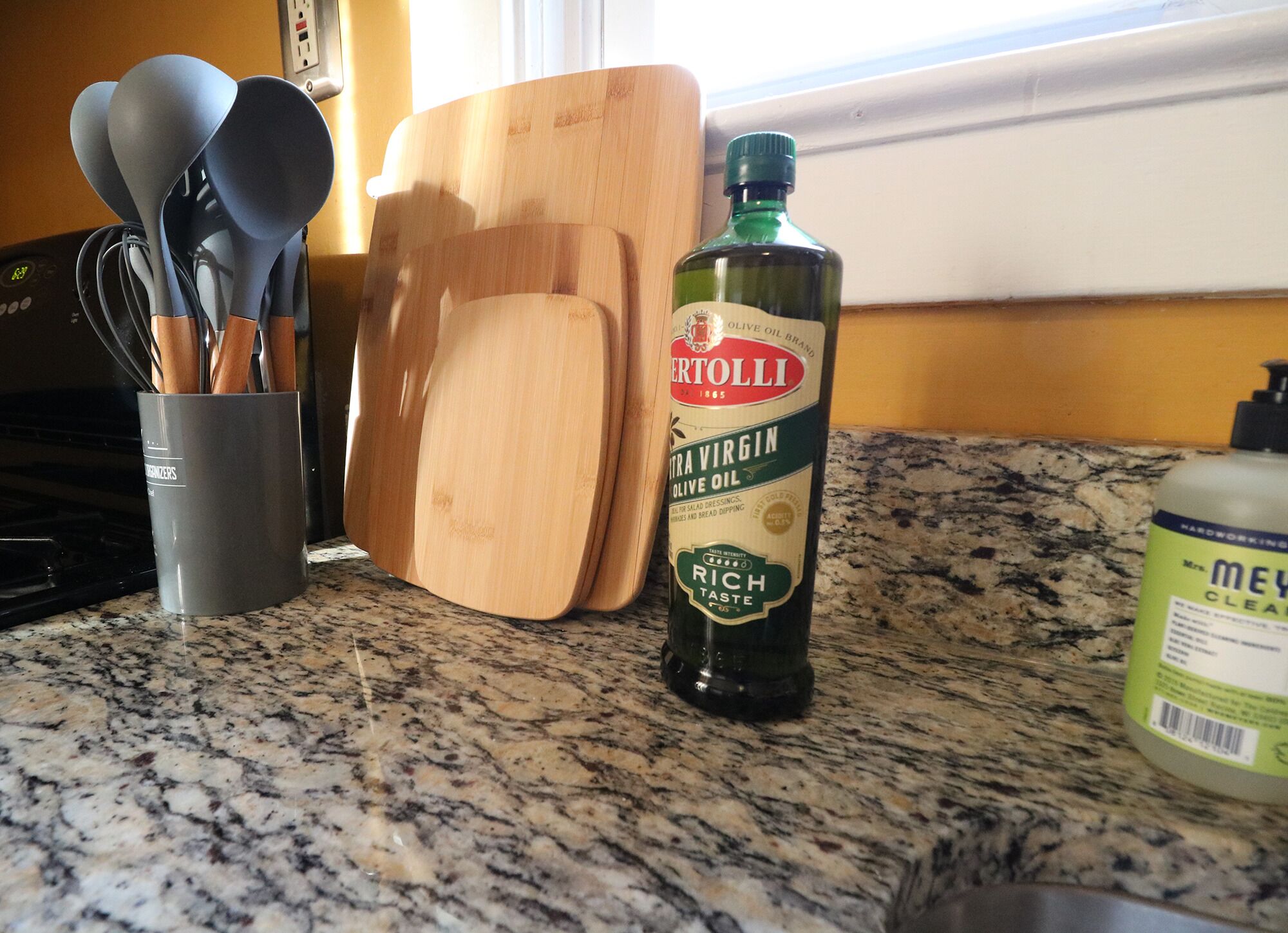 Una encimera de cocina con una botella de aceite de oliva extra virgen, una tabla de cortar y un recipiente para utensilios.