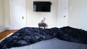 A bedroom with a black furry blanket, a mounted TV, and a bedside table with a lamp. - ★ Downtown Princeton Elegance ★ (Princeton)