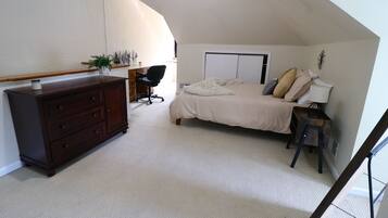 A bedroom with a bed, dresser, desk, chair, and a small table with a lamp.