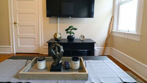 A room with a flat-screen TV mounted on the wall, a wooden tray with decorative items, a potted plant, and a window with blinds. - ★ Downtown Princeton Elegance ★ (Princeton)