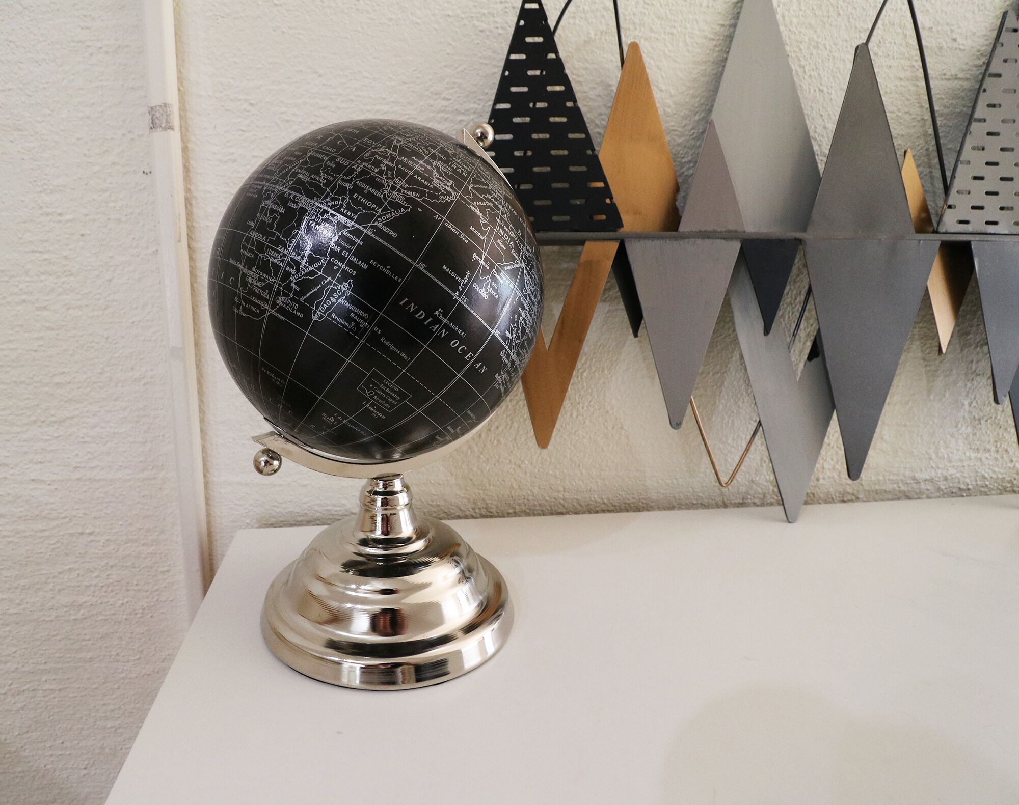 En globus på en metalfod foran en væg med geometriske dekorationer.