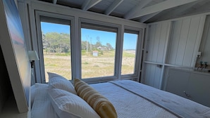 Une chambre avec un grand lit, deux fenêtres et une vue sur un espace verdoyant.