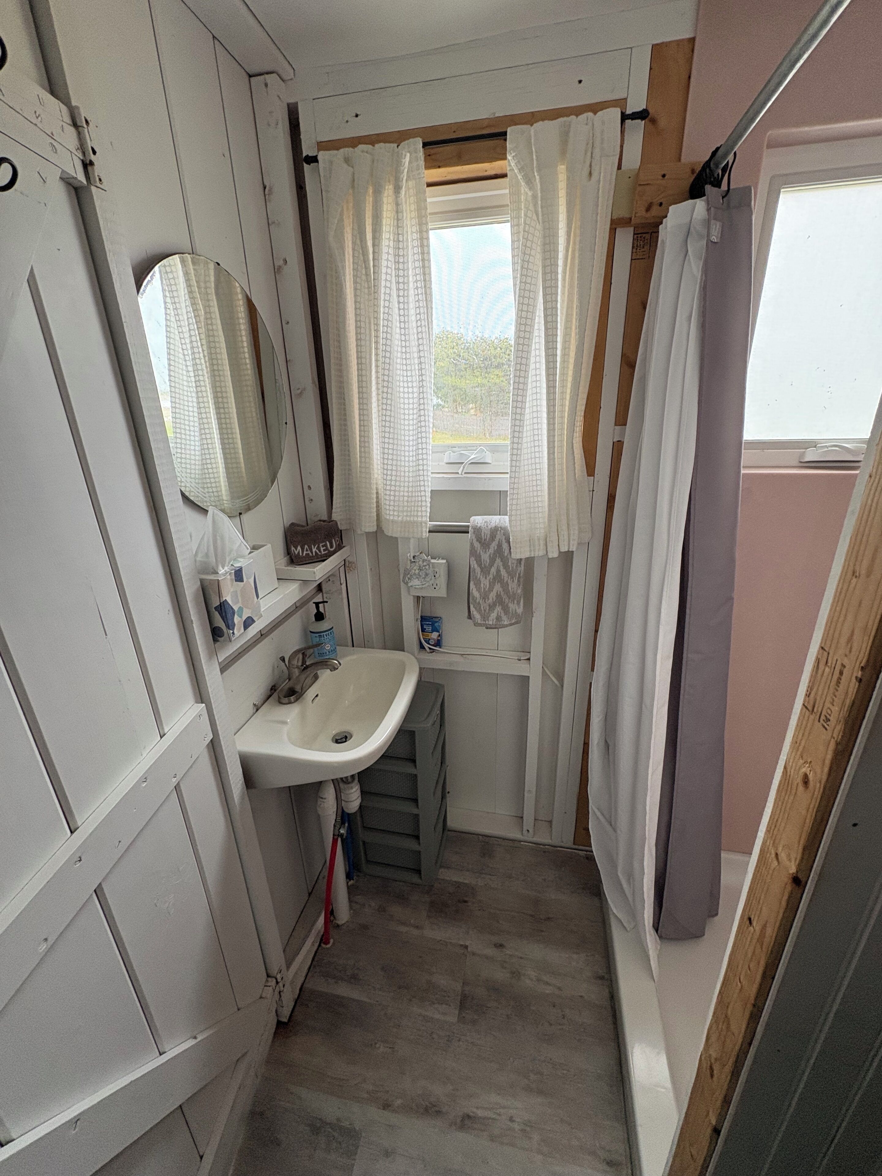 Une petite salle de bain comprenant un lavabo, un miroir et une fenêtre avec des rideaux.