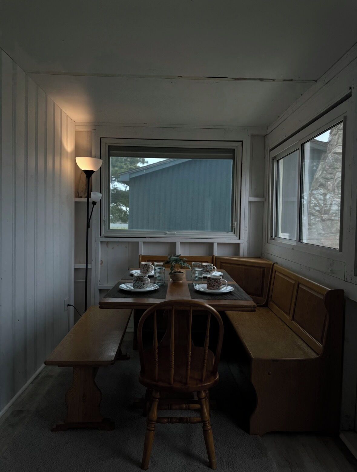Un coin repas avec une table dressée pour quatre personnes, un banc et une lampe.