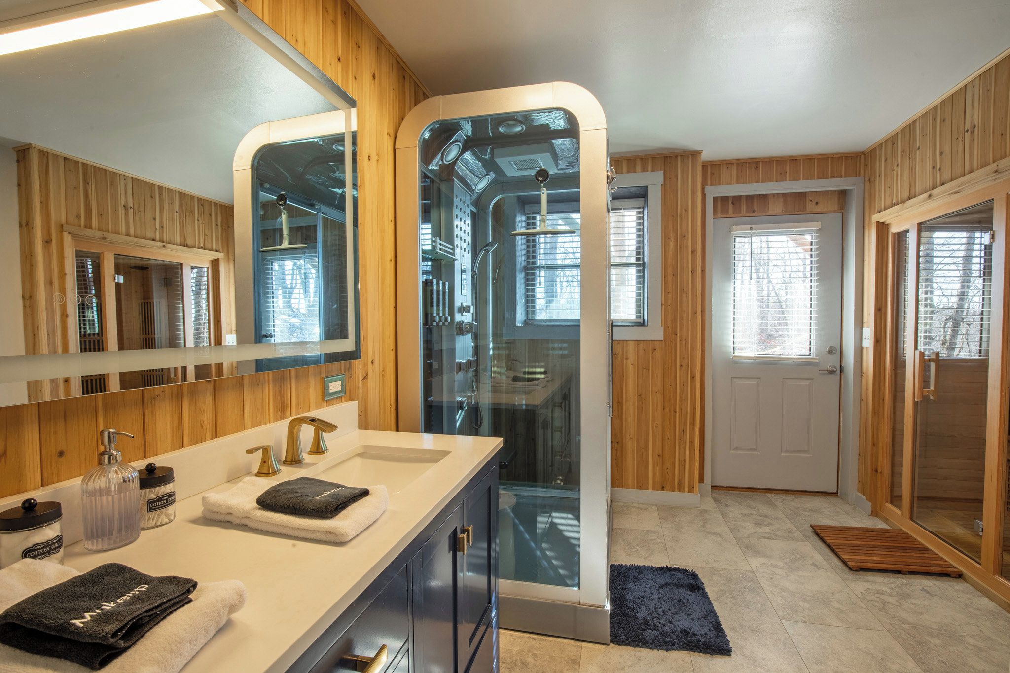 A modern bathroom with a glass-enclosed shower, wooden paneling, and a white sink with gold fixtures.