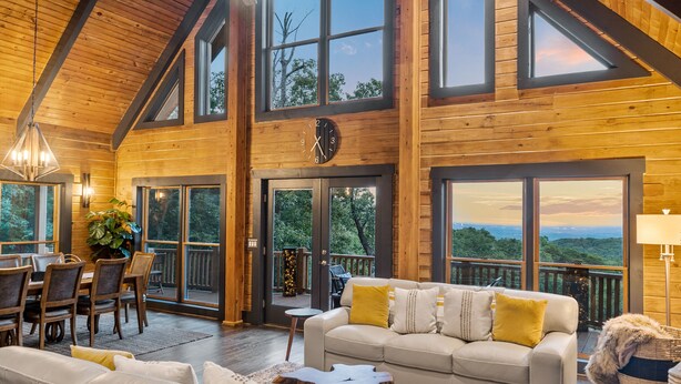 A spacious wooden interior with a large dining area, a cozy seating area with a sofa and cushions, and large windows offering a view of the outdoors. - Luxe Mountain getaway only 15 minutes from the city! (Greenville)