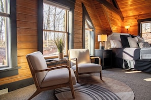 Une pièce confortable avec un lit, deux chaises, une table de chevet et une lampe.