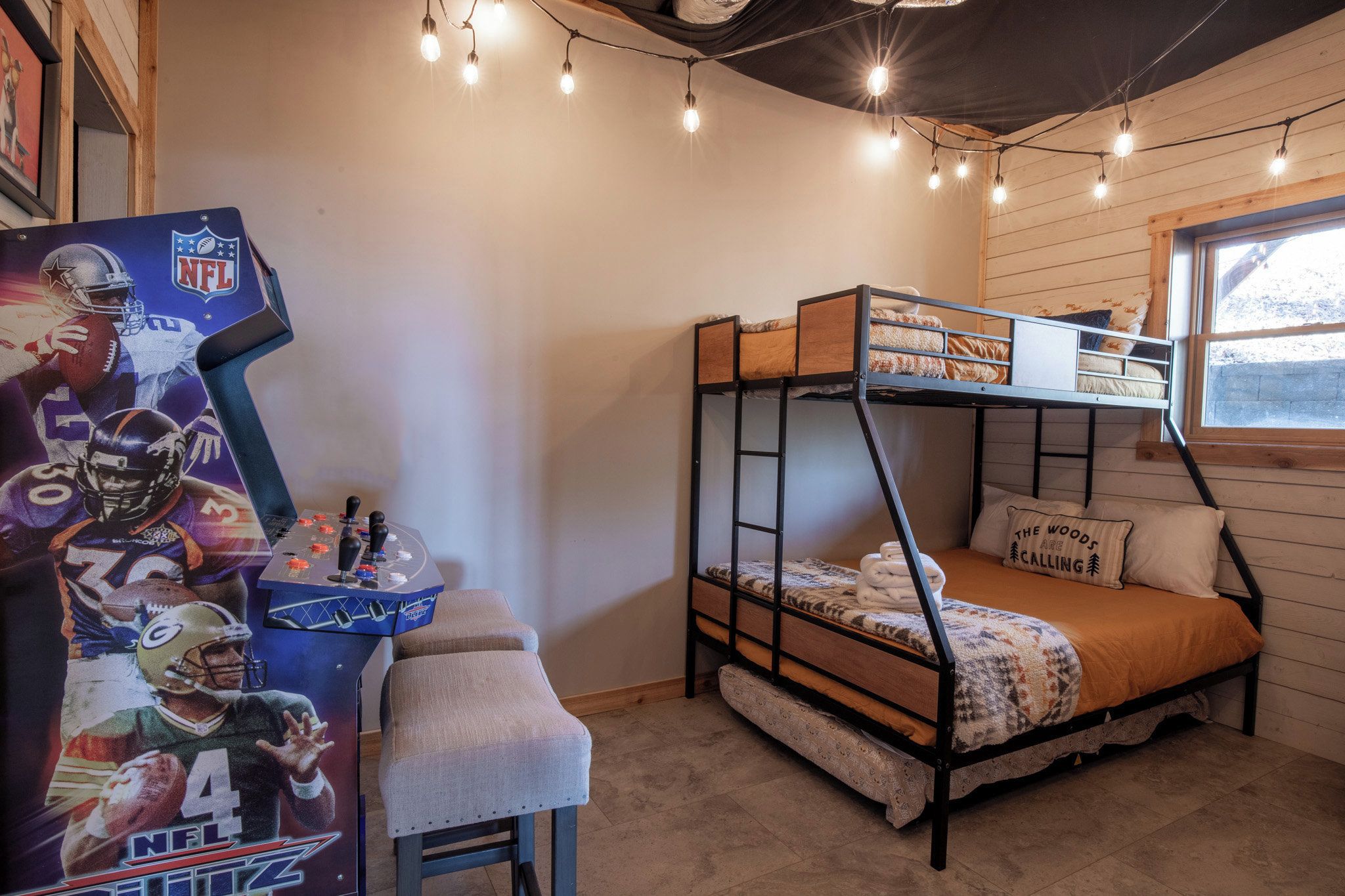 A bunk bed with a window, a desk with a chair, and string lights.