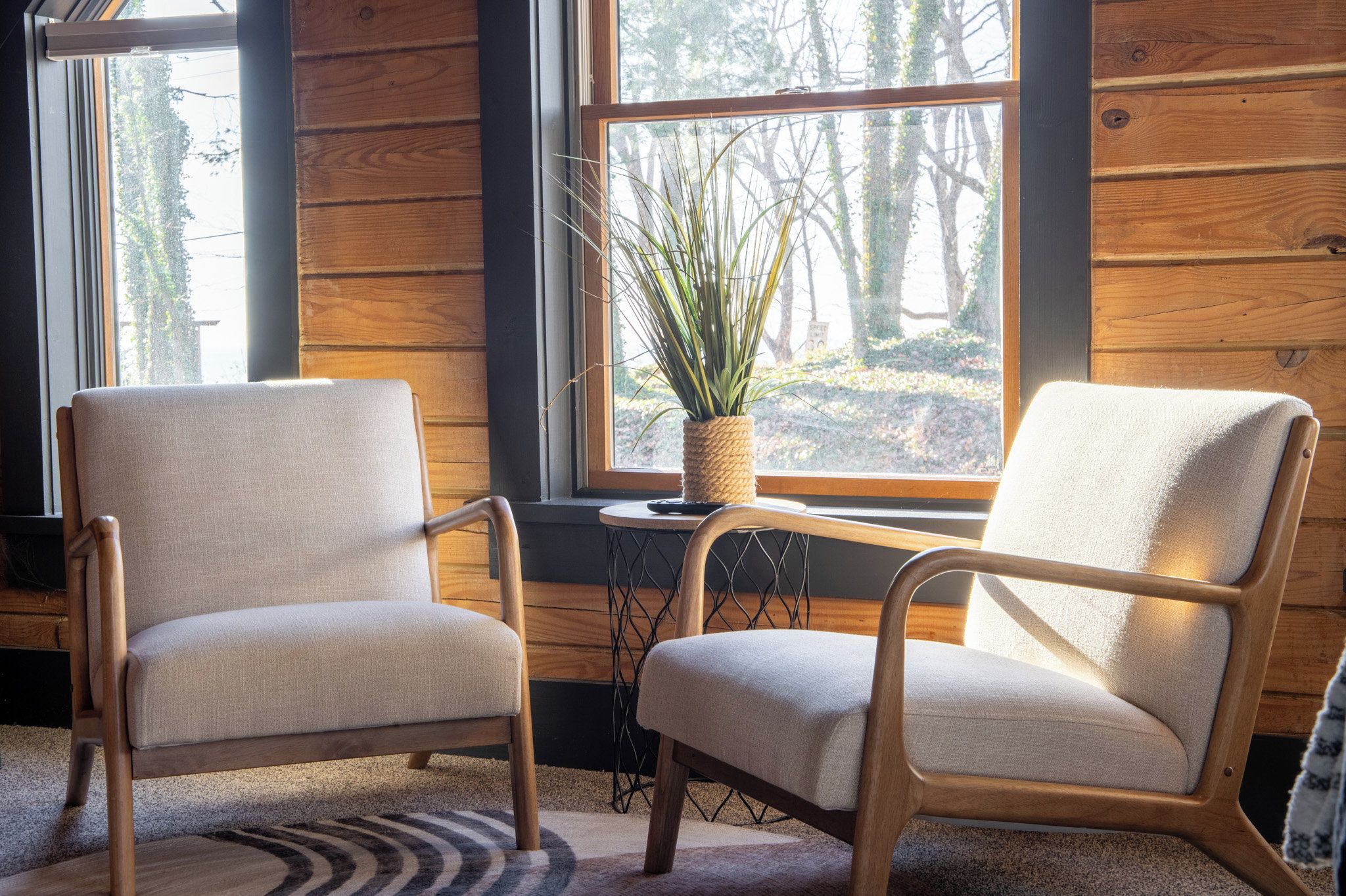 Deux fauteuils à assise tissée, une petite table sur laquelle est posée une plante en pot et une fenêtre donnant sur des arbres.