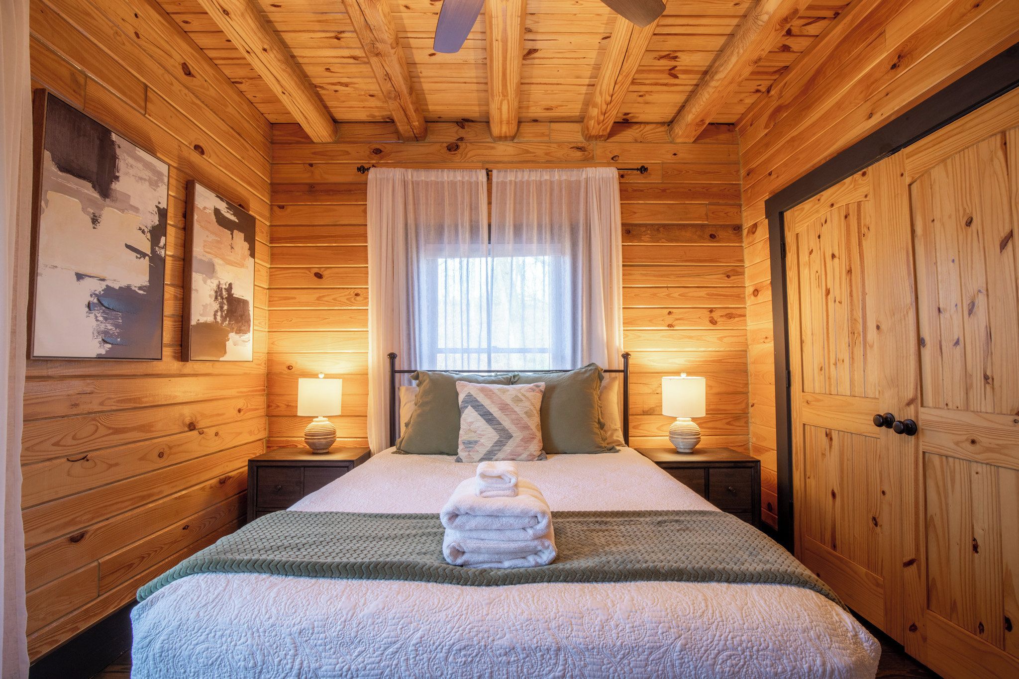 Una habitación con paneles de madera, una cama, dos mesitas de noche y un ventanal con cortinas.