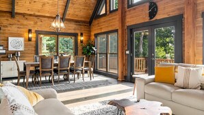 A spacious wooden cabin with a dining area, a living room with a sofa and coffee table, and large windows offering views of the outdoors. - Luxe Mountain getaway only 15 minutes from the city! (Greenville)