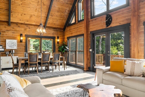 Eine geräumige Holzblockhütte mit Essbereich, einem Wohnzimmer mit Sofa und Couchtisch sowie großen Fenstern mit Blick ins Freie.