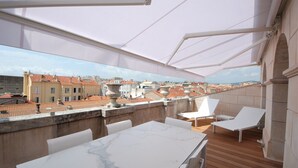 A rooftop terrace with a view of the cityscape, featuring a marble table, white chairs, and a stone urn. - Luxury Duplex in the Heart of Cannes (Cannes)