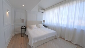A modern bedroom with a large bed, a nightstand, a lamp, and a window with sheer curtains. - Luxury Duplex in the Heart of Cannes (Cannes)