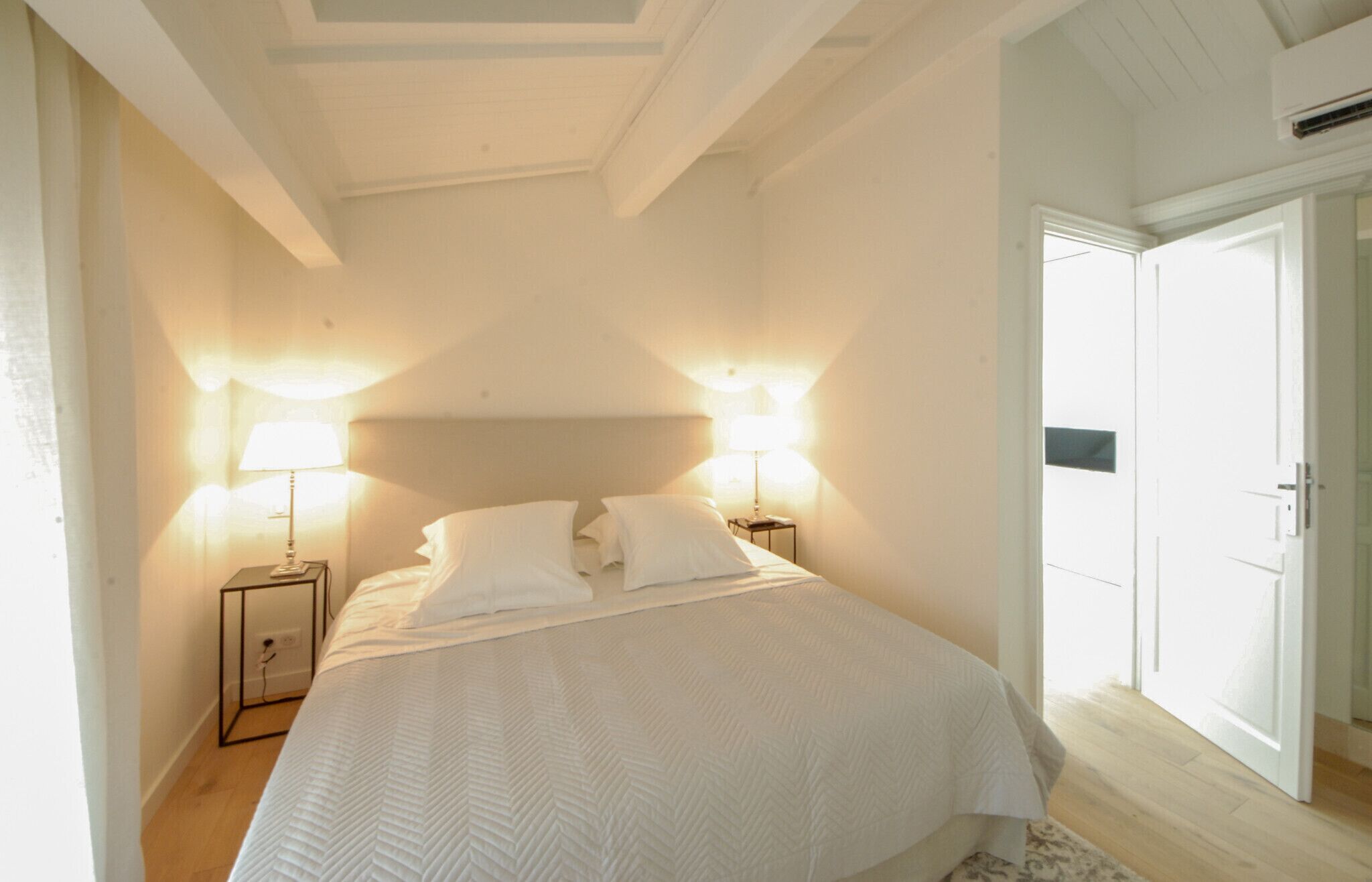 Une chambre avec un grand lit, deux lampes de chevet et une porte donnant sur une autre pièce.