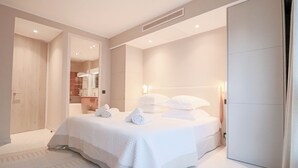 A modern hotel room with a large bed, a walk-in closet, and a bathroom visible through an open door.