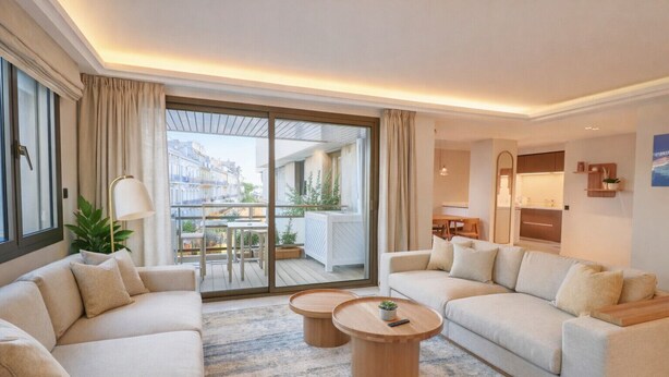 A modern living room with two sofas, a coffee table, and a view of a balcony with outdoor furniture.
