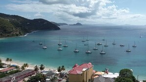 Une zone côtière où de nombreux bateaux sont amarrés, une plage bordée de palmiers et des bâtiments au premier plan.