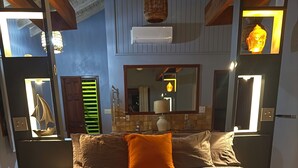 Un lit avec une literie à motifs, un oreiller orange vif et un miroir au-dessus.