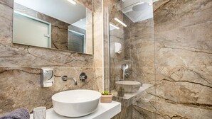Une salle de bain moderne avec un lavabo en marbre, une douchette à main et une douche à parois de verre.