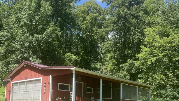 A red single-story building with a covered porch and a garage. - CURRENTLY UNDER REPAIR (Deersville)