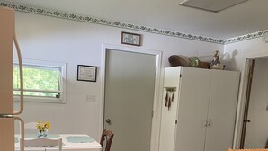 A small, compact room with a dining table, two chairs, a white wardrobe, and a door leading to another room. - CURRENTLY UNDER REPAIR (Deersville)