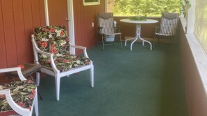 A covered porch with a green carpet, white chairs with floral upholstery, a small table, and a door. - CURRENTLY UNDER REPAIR (Deersville)