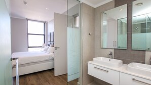 A modern bathroom with a glass shower enclosure, a double sink vanity, and a large mirror. - CGRSA Apartment Sandton (Sandton)