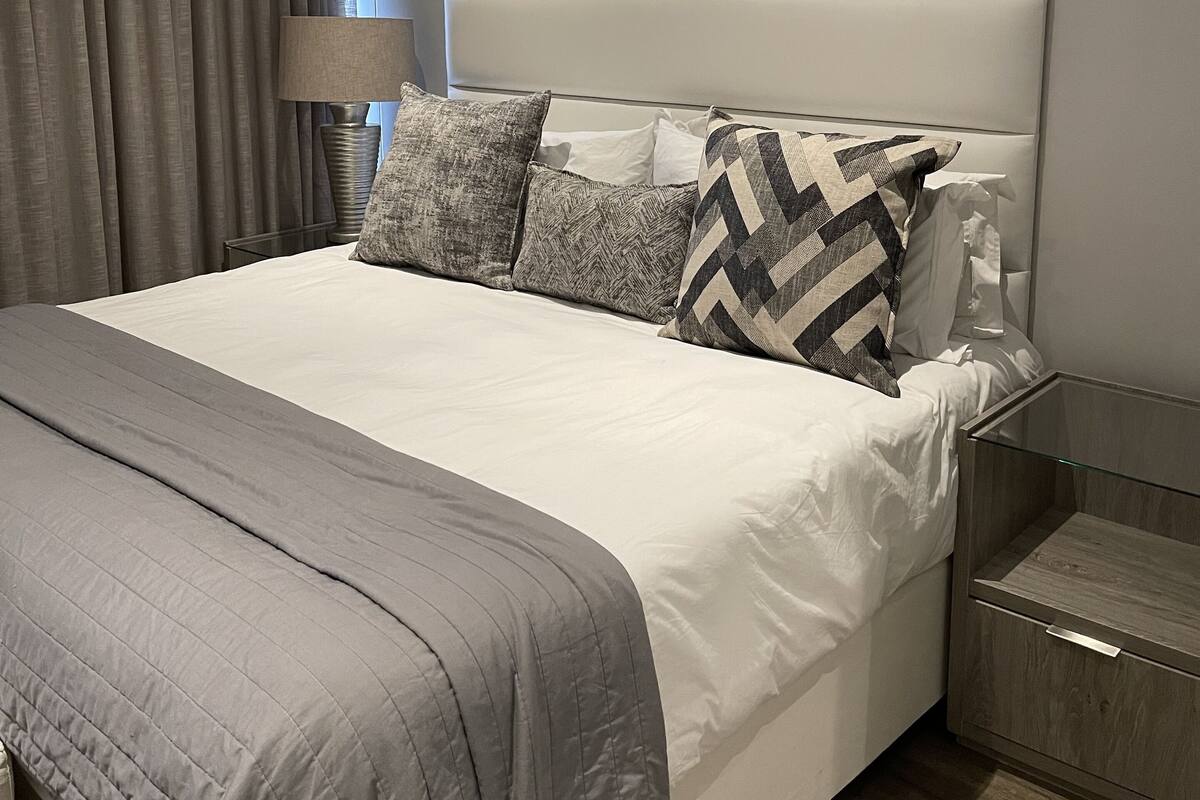 A modern bedroom with a large bed, grey bedding, and a headboard.