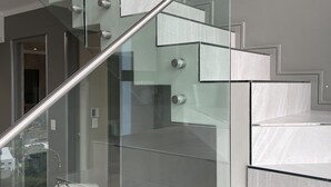 A modern staircase with glass railings and a metal handrail, leading to a room with a glass table and chairs. - CGRSA Apartment Sandton (Sandton)