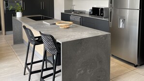 A modern kitchen with a central island, black cabinetry, stainless steel appliances, and a built-in oven. - CGRSA Apartment Sandton (Sandton)