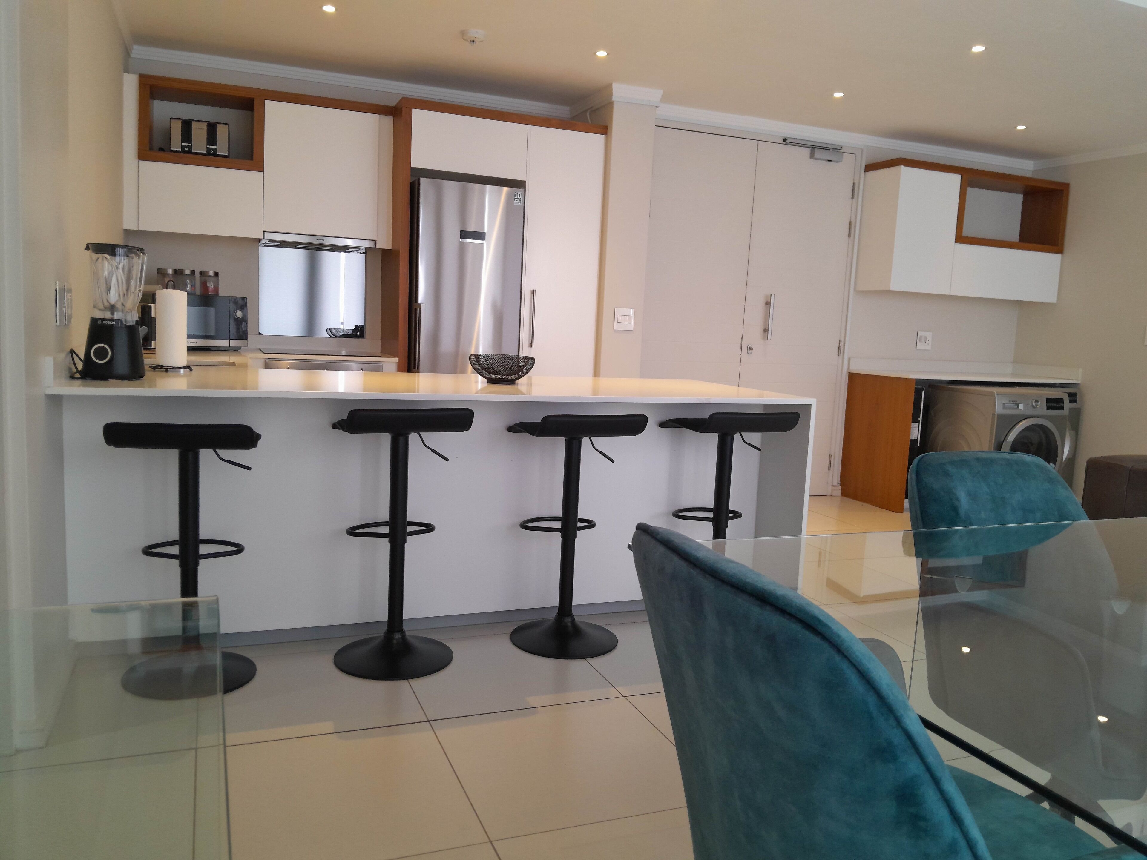 A modern kitchen with a central island, bar stools, and a washing machine.