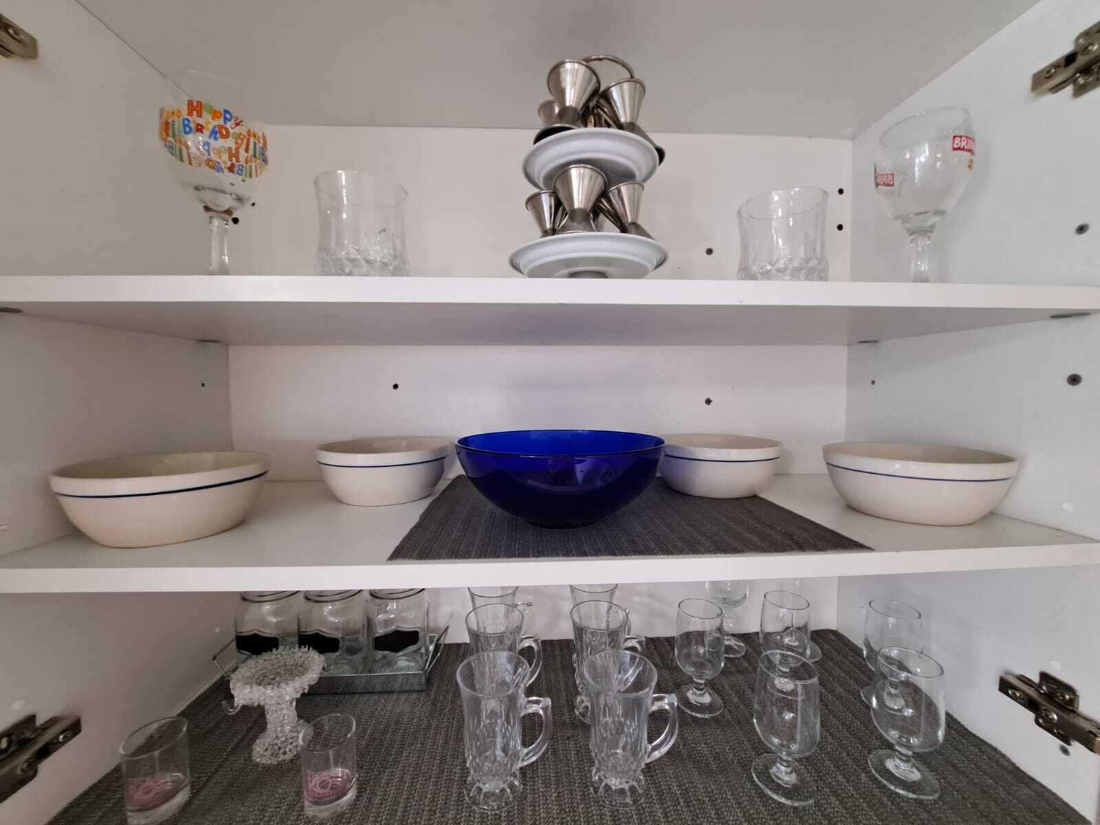 A kitchen with white shelves, a blue bowl, and various glassware.