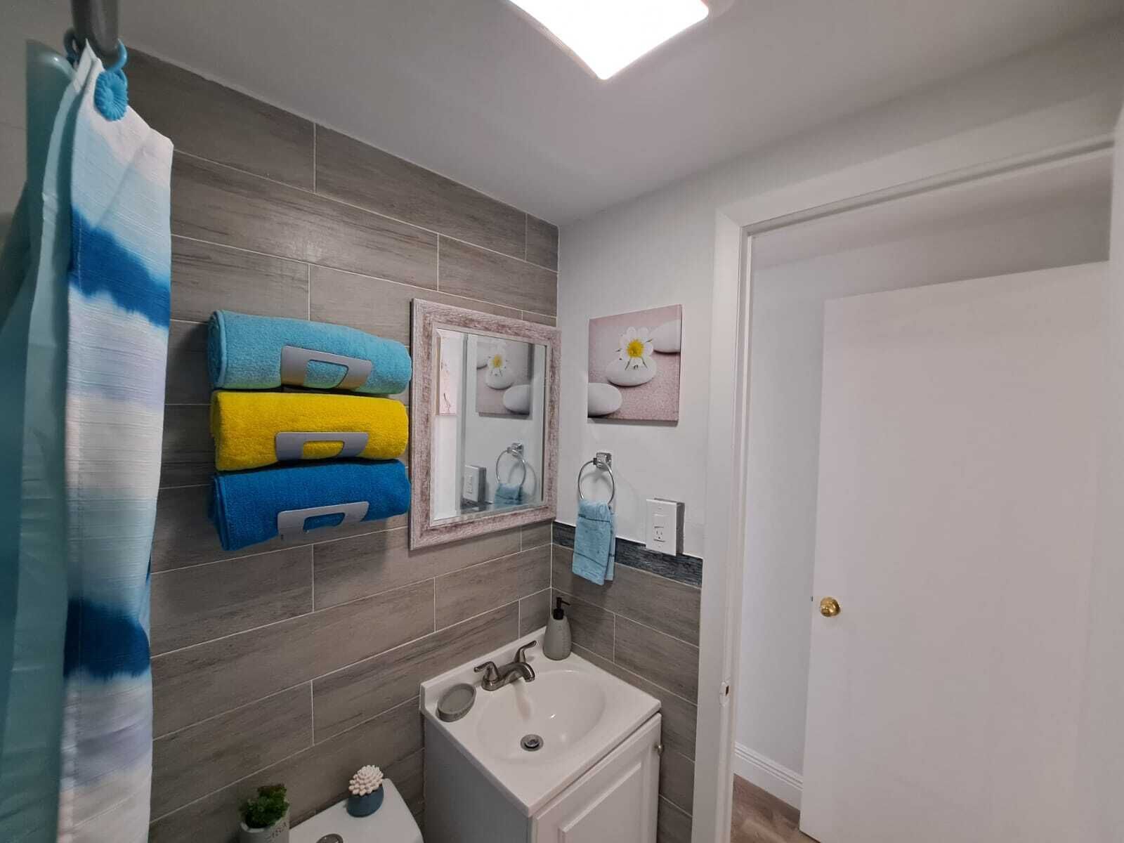 A bathroom with grey tiles, a white sink, a mirror, and a towel rack with folded towels.