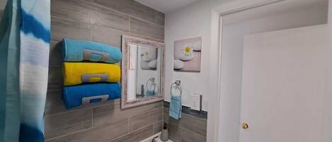 A bathroom with grey tiles, a white sink, a mirror, and a towel rack with folded towels.