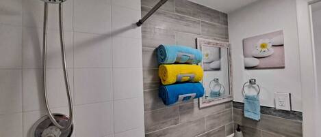 A modern bathroom with a shower, a sink, and a toilet. There are towels stacked on a rack and a framed picture on the wall.