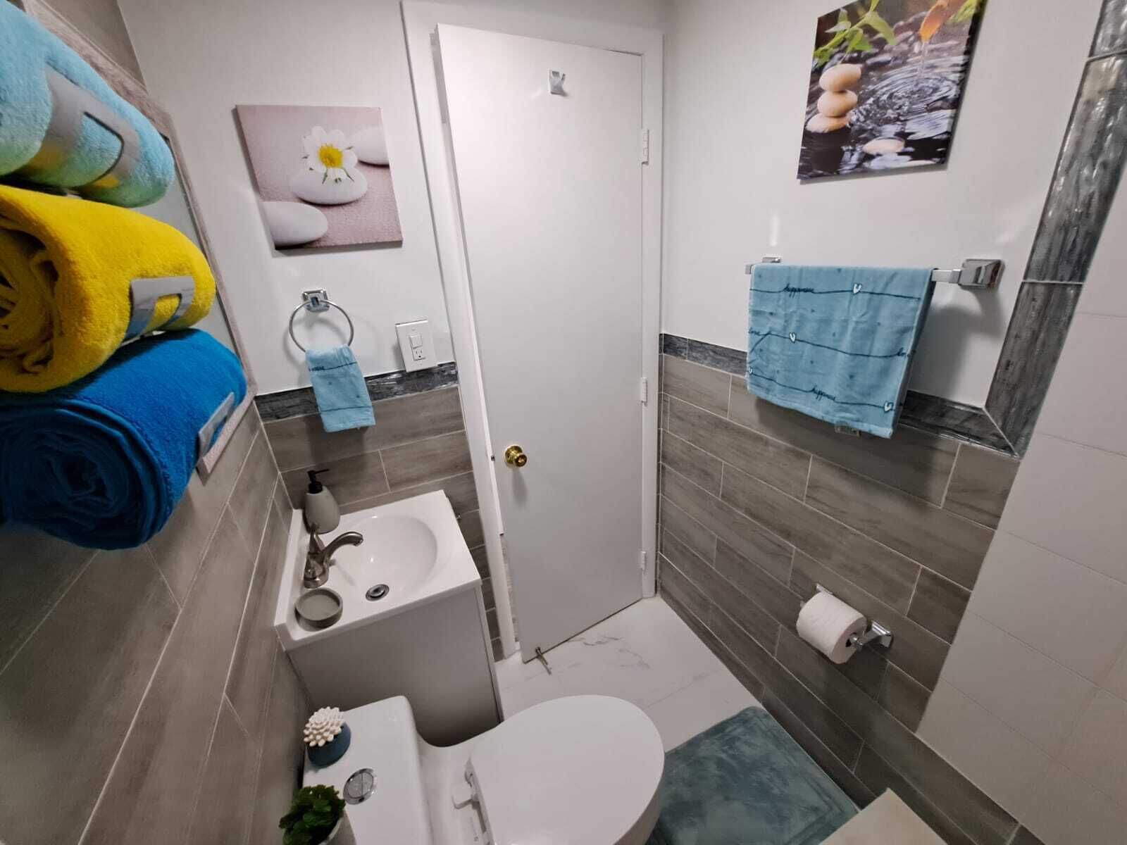 Une petite salle de bain comprenant des toilettes, un lavabo et un espace douche. On peut voir des serviettes et des articles de toilette.