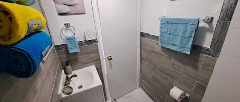 Une petite salle de bain comprenant des toilettes, un lavabo et un espace douche. On peut voir des serviettes et des articles de toilette.