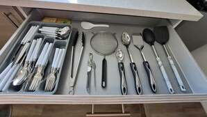 Un cassetto della cucina con utensili da cucina ordinatamente disposti, tra cui coltelli, cucchiai, spatole e pinze.