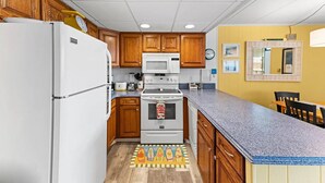 A compact kitchen with wooden cabinets, a white refrigerator, a microwave, an oven, and a granite countertop. - Hidden Gem Oceanview! 3BD/2BR, Steps to the beach! (Ocean City)