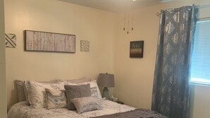 A bedroom with a bed, a ceiling fan, a nightstand, a lamp, and a window with curtains. - Relaxing - Two Bedroom Suite in Red Deer (Red Deer)