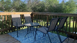 A deck with a round table and four chairs, surrounded by a wooden railing and a patterned rug. - Relaxing - Two Bedroom Suite in Red Deer (Red Deer)