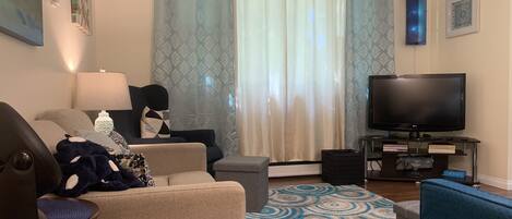Una sala de estar con sofá, sillón, televisor y alfombra estampada.