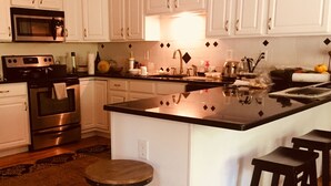 Una cucina moderna con mobili bianchi, elettrodomestici in acciaio inossidabile, un'isola centrale con sgabelli e un tappeto decorativo sul pavimento.