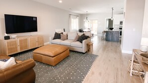 Un salon moderne avec un canapé, un pouf et un téléviseur à écran plat.