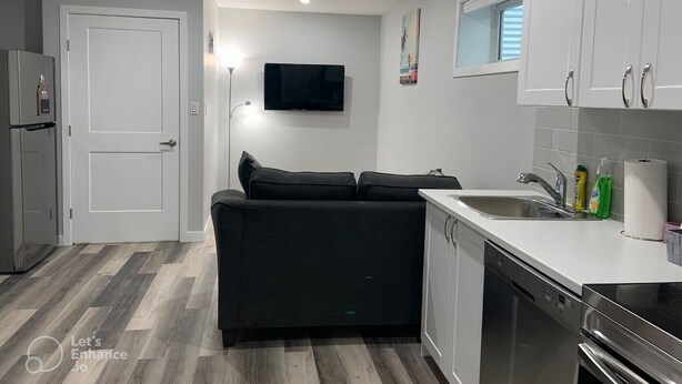Een moderne keuken met witte kasten, een ingebouwde vaatwasser, een kookplaat en een flatscreen televisie aan de wand.