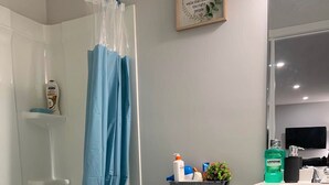 Een moderne badkamer met een wit toilet, een blauw douchegordijn, een fles Listerine en een klein plantje op de wastafel.