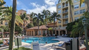 A pool area with lounge chairs and palm trees, surrounded by multi-story buildings with balconies. - Modern cozy feeling Next to Beach and Aventura Mall (Miami)