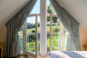 A bedroom with a large skylight and curtains, a bed, and a view of a green landscape. - Trewhiddle Villa 07 -  a trewhiddle that sleeps 6 guests  in 3 bedrooms (Saint Austell)