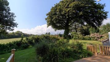 A wooden deck leading to a grassy area with a large tree and dense shrubbery.
